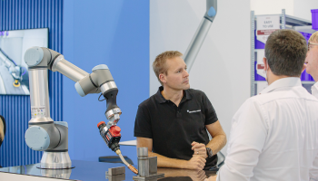 Hier sieht man ein Cobot von Universal Robots und neben dem Cobot steht ein Mitarbeiter von Universal Robots und spricht mit Kunden.